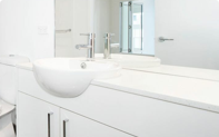 Banheiro completo todo branco com torneira niquel e espelho grande.
